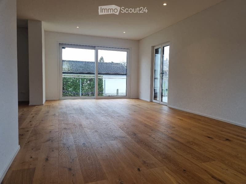 Empty room with wooden flooring, large sliding glass doors, and white walls.