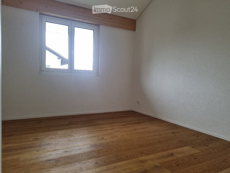 Empty room with wooden flooring and white walls, featuring a single window with white frame and a visible electrical outlet on the wall.