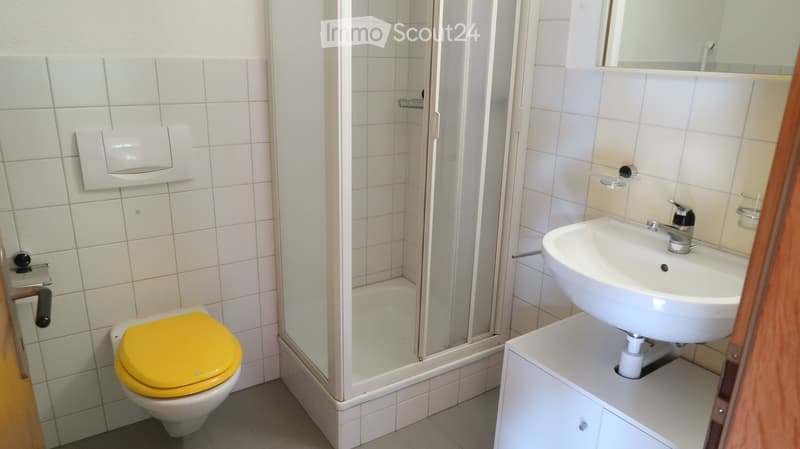 Bathroom with white tiled walls, a yellow toilet seat, a white sink with a chrome faucet, and a glass-enclosed shower area.