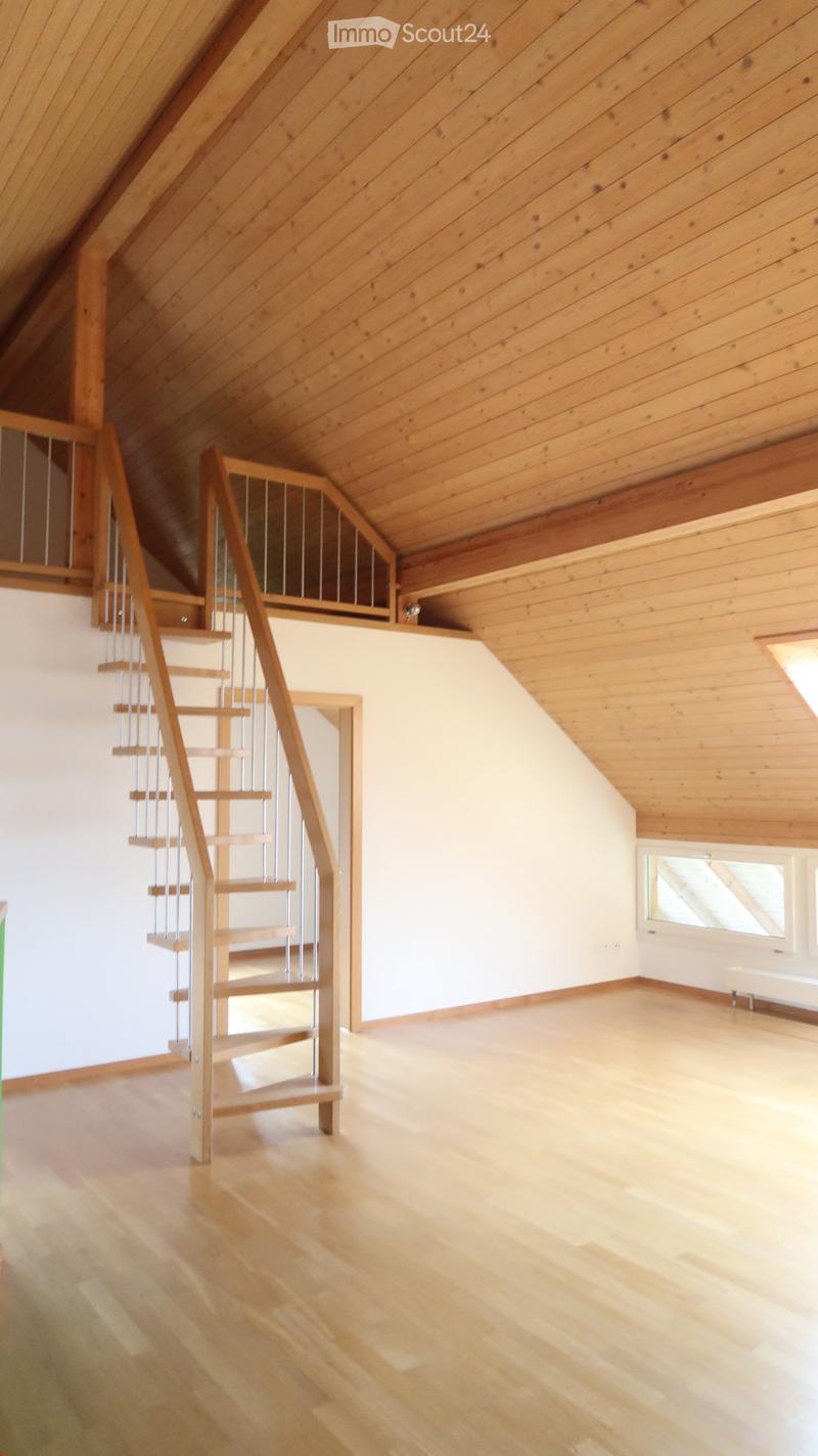 Empty attic space with wooden floors and walls, featuring a wooden staircase leading to an upper level and skylight windows providing natural light.