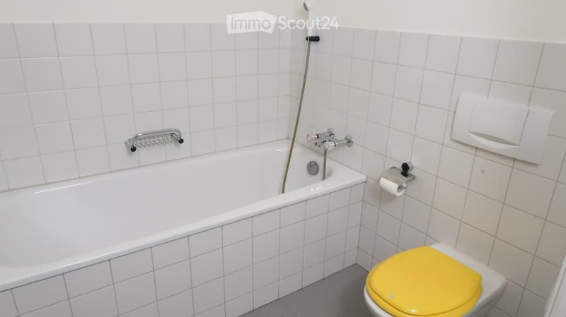 Bathroom with white tiled walls, a bathtub, a toilet with a yellow seat, a faucet, and a toilet paper holder.