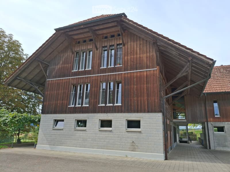 Two-story wooden house with a stone base, large windows, and a covered entrance area.