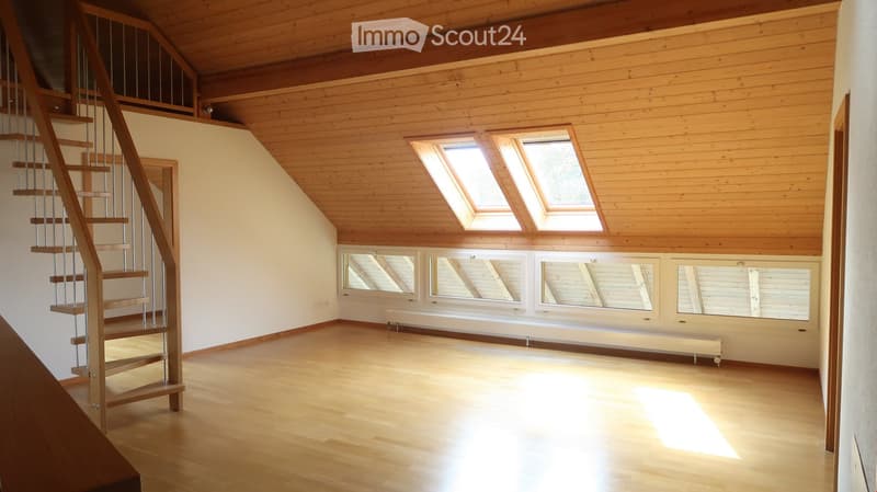 Bright, open attic space with wooden floors, exposed wooden ceiling beams, skylights, and large windows. A modern spiral staircase leads to an upper level.