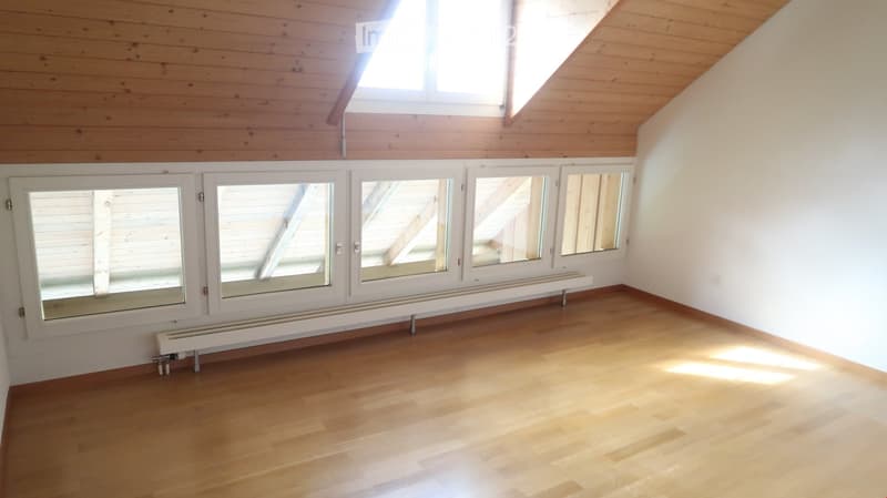Empty room with wooden flooring, white walls, large windows, and a radiator. No furniture or equipment present.