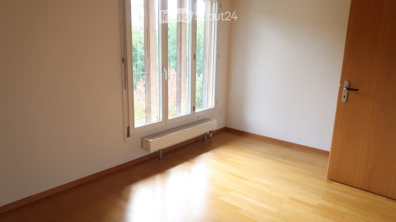 Empty room with wooden flooring, large windows, and a radiator. No furniture or equipment present.