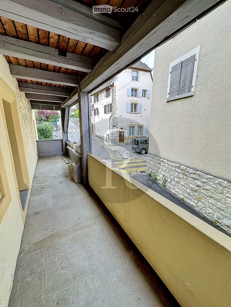Narrow covered walkway with stone walls, wooden beams, and a view of a street with a parked van and a traditional building.