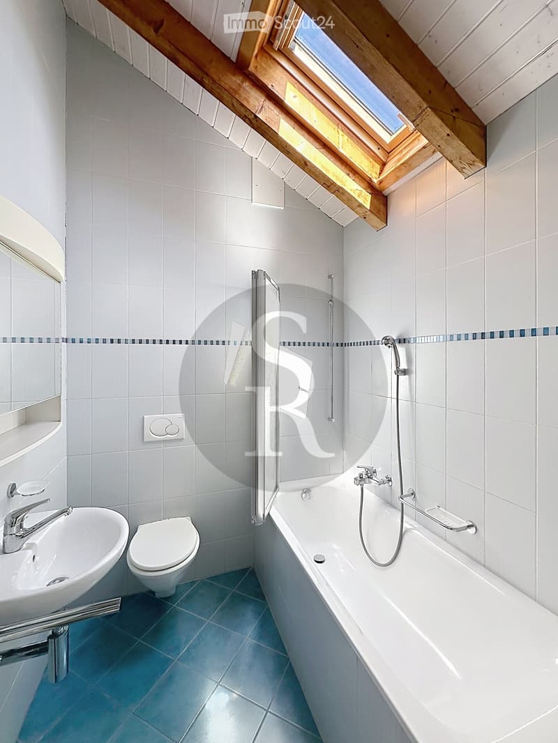 Modern bathroom with white tiles, a bathtub, toilet, sink, and a large skylight window providing natural light.