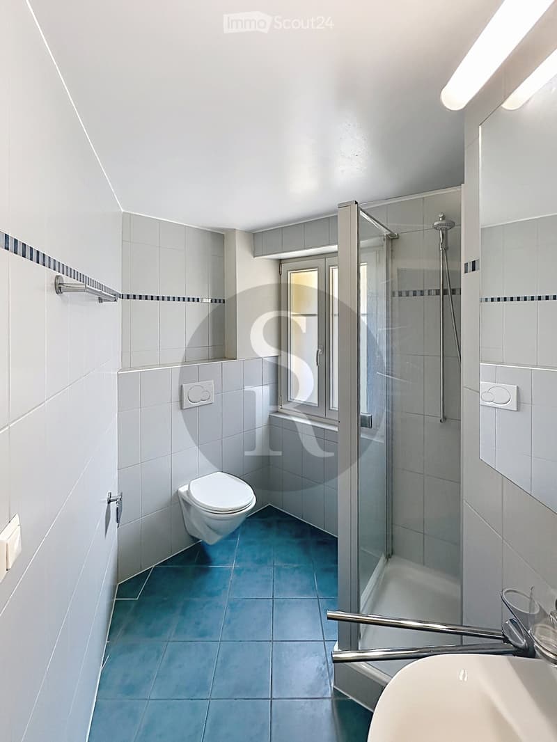 Modern bathroom with white tiles, blue floor, toilet, sink, and glass-enclosed shower area.