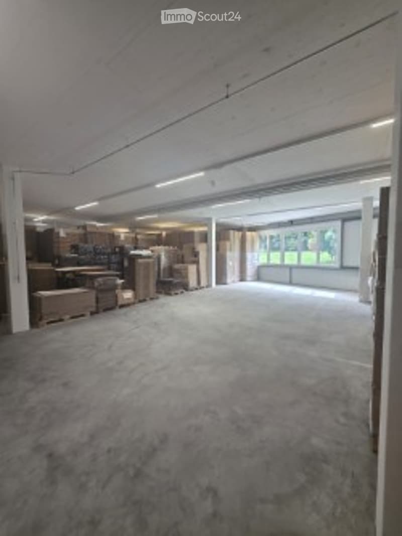 Empty garage with concrete floor, exposed wooden beams, and large windows at the far end.