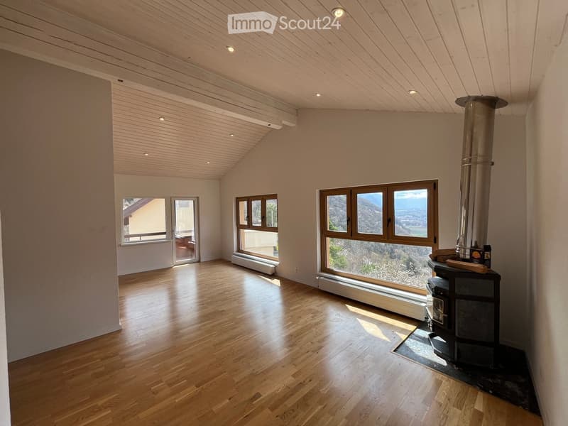 Empty room with wooden flooring, large windows offering scenic views, and a fireplace with a chimney.