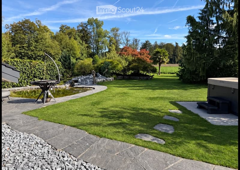 Well-maintained garden with a lawn, stone pathways, a small pond, a barbecue area, and a hot tub.