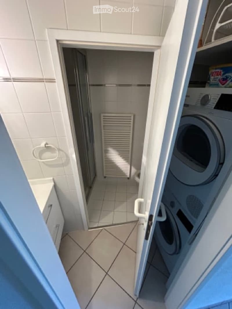 Bathroom with a radiator, washing machine, and a shower stall visible through an open door.