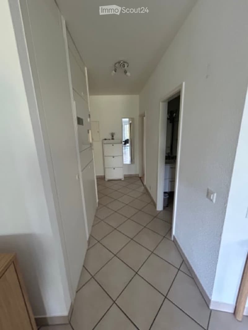 A narrow hallway with tiled flooring and white walls, featuring a ceiling light fixture and several doors leading to different rooms.