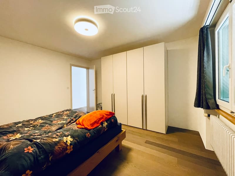 Bedroom with a single bed, orange pillow, white wardrobe, and a window with curtains.