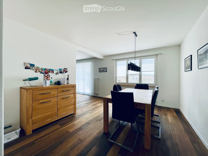 Bright dining area with wooden floor, large window, modern wooden dresser, dining table with chairs, and decorative items on dresser.