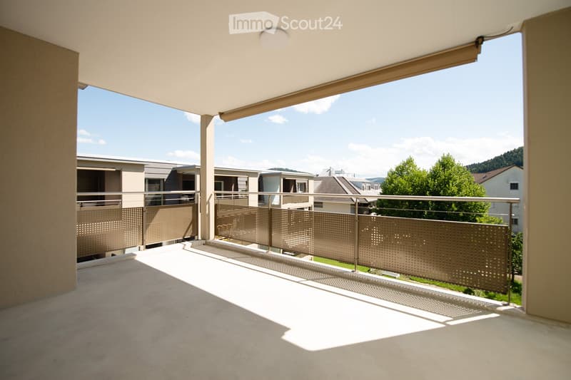 Modern balcony with metal railings, concrete floor, and a view of neighboring buildings and greenery.