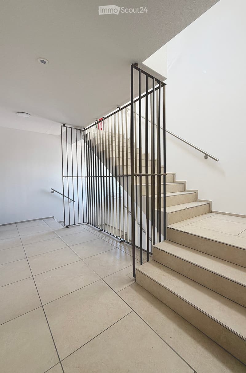 Modern hallway with tiled floor, white walls, and a staircase with beige steps and a black metal railing.