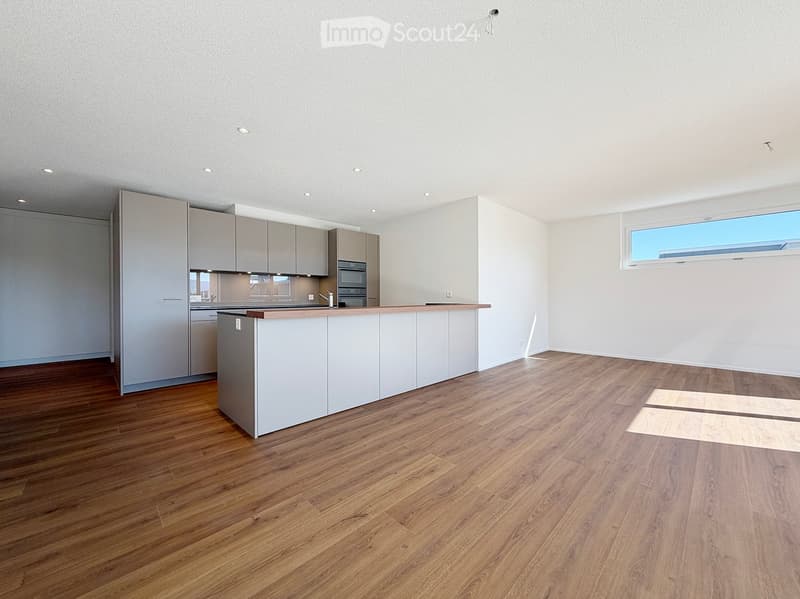 Modern, minimalist kitchen with light grey cabinets, a central island, and wooden flooring. The space is empty, with no appliances or furniture visible.