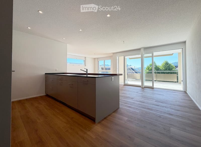Modern kitchen with a central island, sink, and faucet, featuring wooden flooring and large windows with a view of the outdoors.