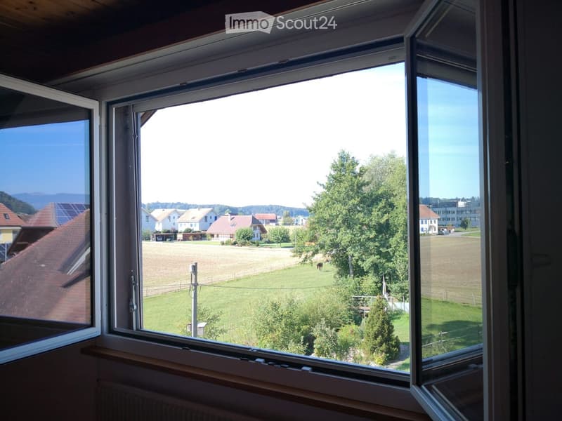 View from a room with large windows showing a rural landscape with fields, houses, and trees.