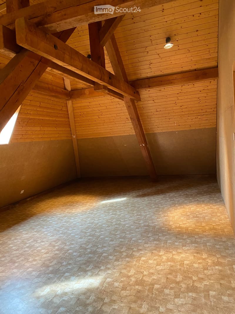 Empty room with wooden beams, exposed wooden ceiling, and tiled floor. Natural light streams in from a window on the left side.