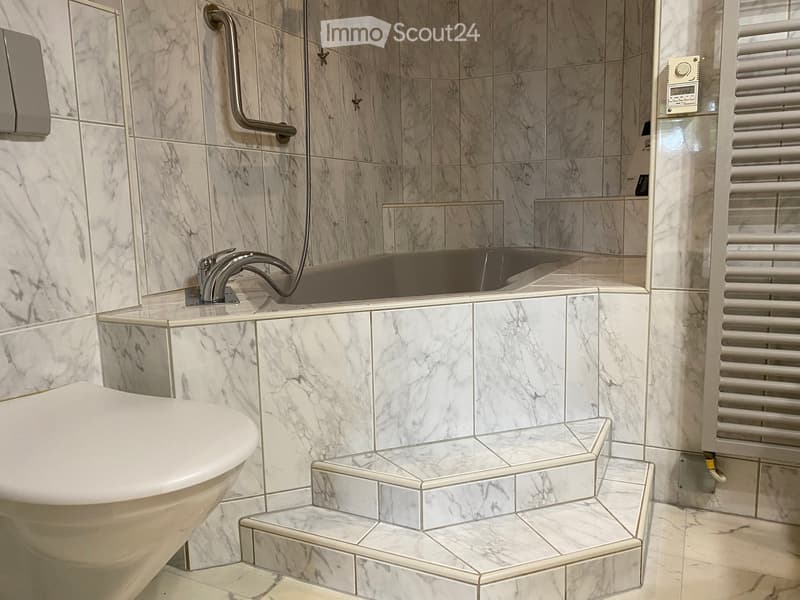 Elegant bathroom with marble tiles, a bathtub, a modern faucet, a mirror, a radiator, and a handrail for accessibility.