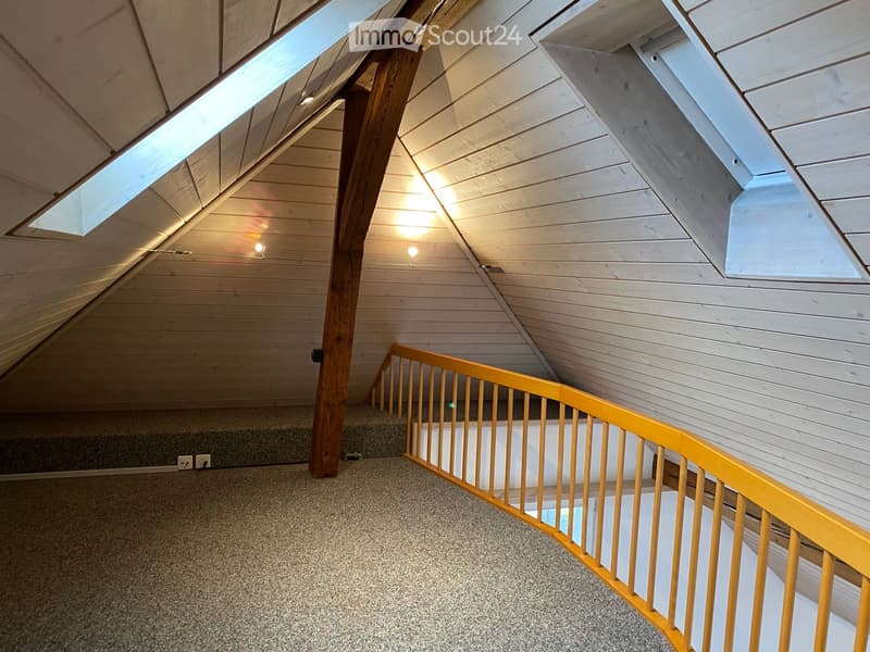 Carpeted staircase with wooden handrail and carpeted steps, leading up to an attic space with exposed wooden beams and skylights.
