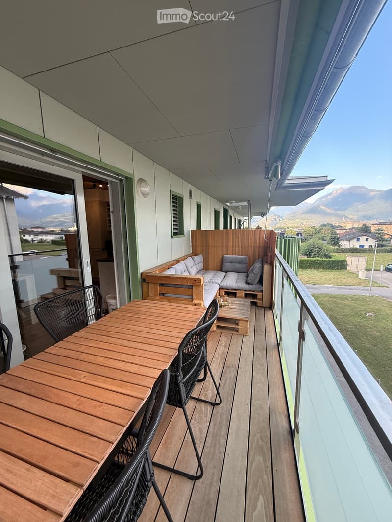 Balcony with wooden decking, outdoor furniture including a table, chairs, sofa, and coffee table, overlooking a scenic mountain view.