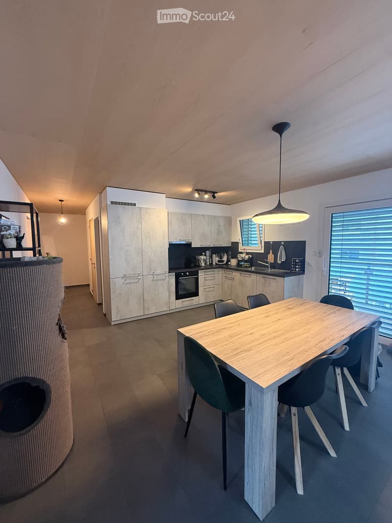 Modern kitchen with light wood cabinets, stainless steel appliances, a central dining table with chairs, and pendant lighting.