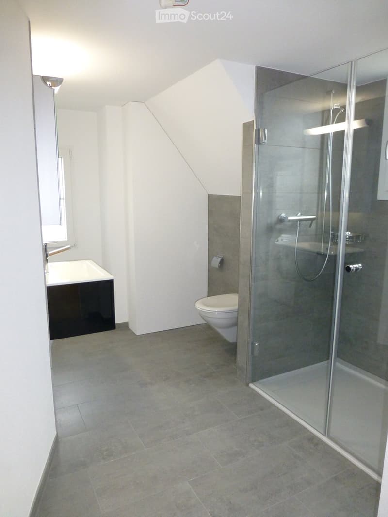 Modern bathroom with a glass-enclosed shower stall, a white toilet, a black sink cabinet, and a window providing natural light.