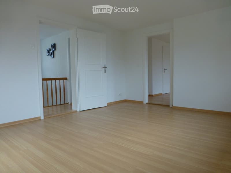 Empty room with light wooden flooring, white walls, and open doorways leading to other rooms. No furniture or equipment is present.