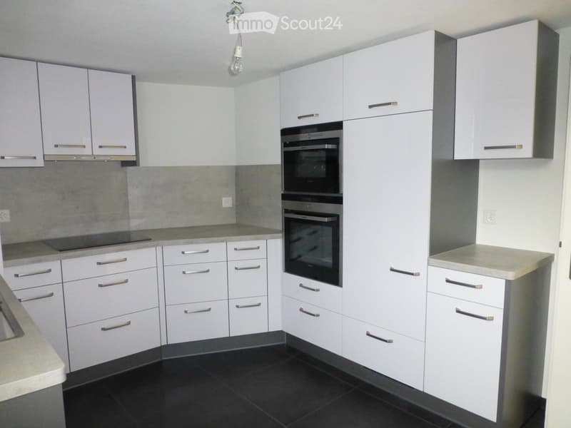Modern kitchen with white cabinets, stainless steel oven, and dark tiled floor.