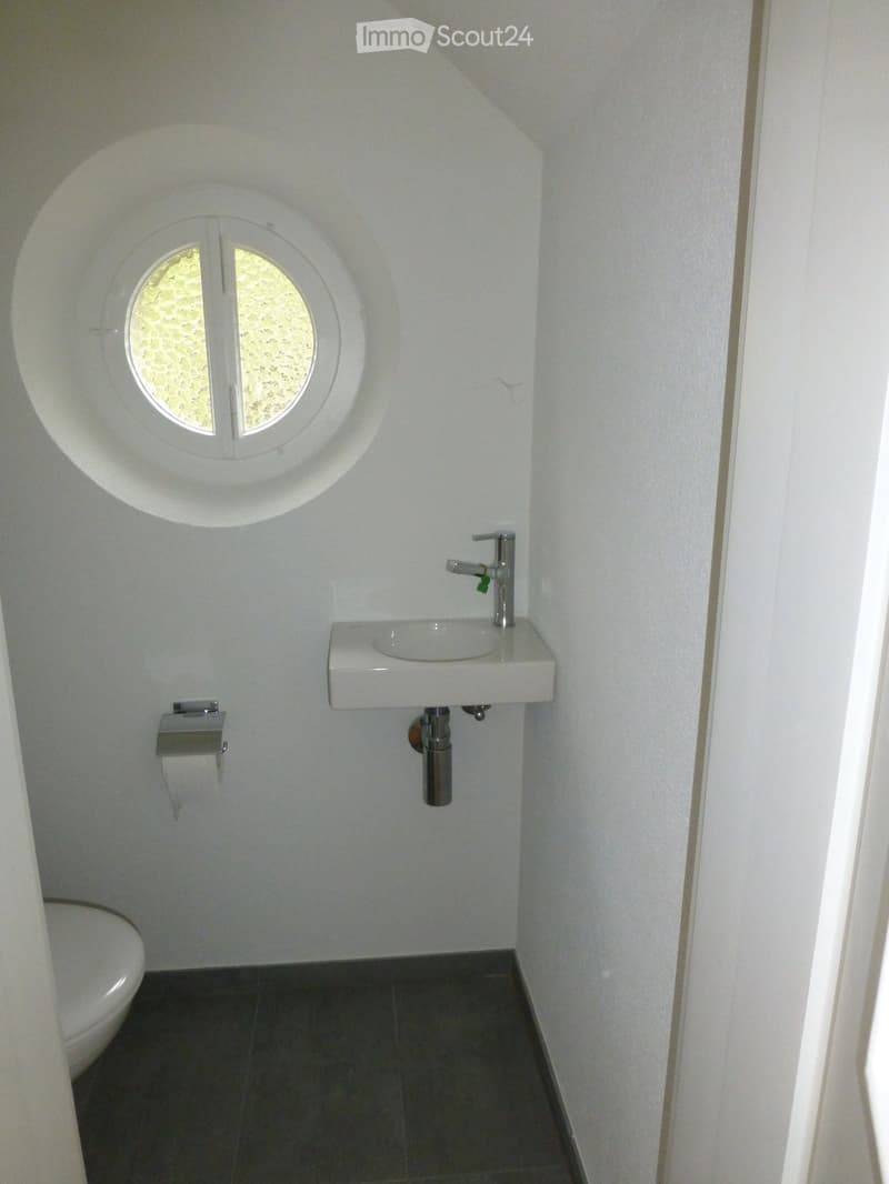 Small bathroom with white walls, dark tiled floor, a white sink with a modern faucet, a toilet, and a round window above the sink.