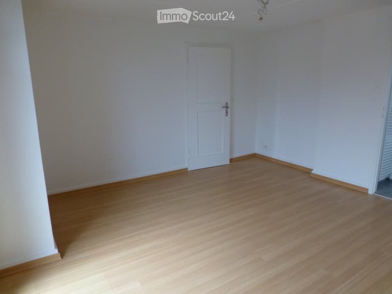 Empty room with light wooden flooring and white walls, featuring a single white door.