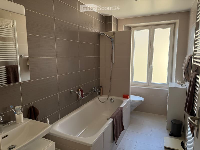 Modern bathroom with a bathtub, toilet, sink, and various accessories including towels, a toothbrush holder, and a radiator.