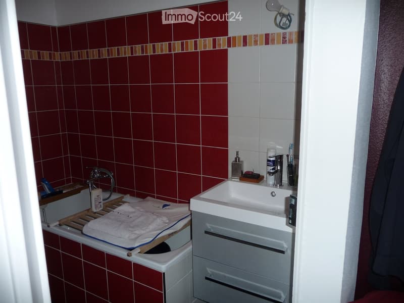Bathroom with red tiled walls, a white bathtub, a white sink with a faucet, and various toiletries on the sink counter.