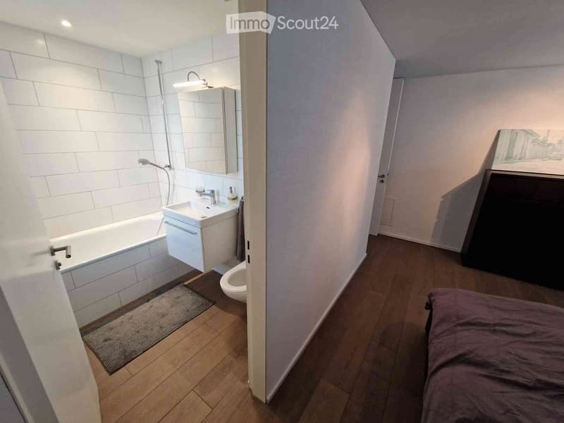Bathroom with white tiled walls, a white bathtub, white sink, and toilet. White ceiling and walls, wooden floor.