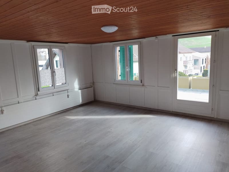 Empty room with wooden flooring, white walls, large windows, and a sliding glass door leading to an outdoor area.