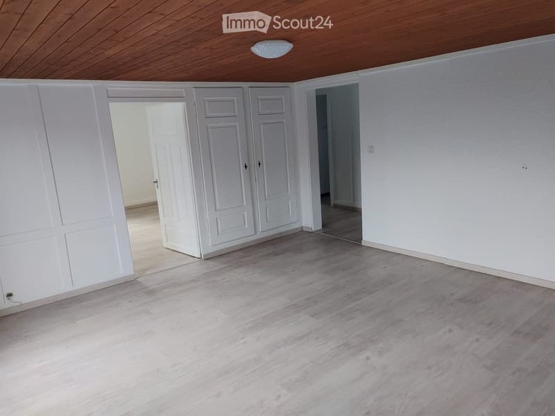 Empty room with light wooden flooring, white walls, and multiple white doors leading to other spaces.