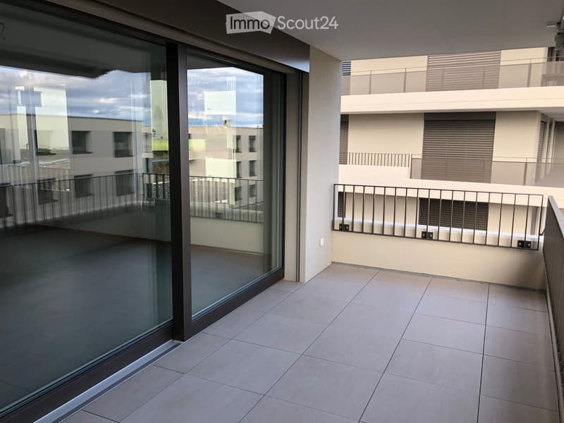 Modern balcony with tiled floor, large glass sliding doors, metal railing, and view of neighboring buildings.