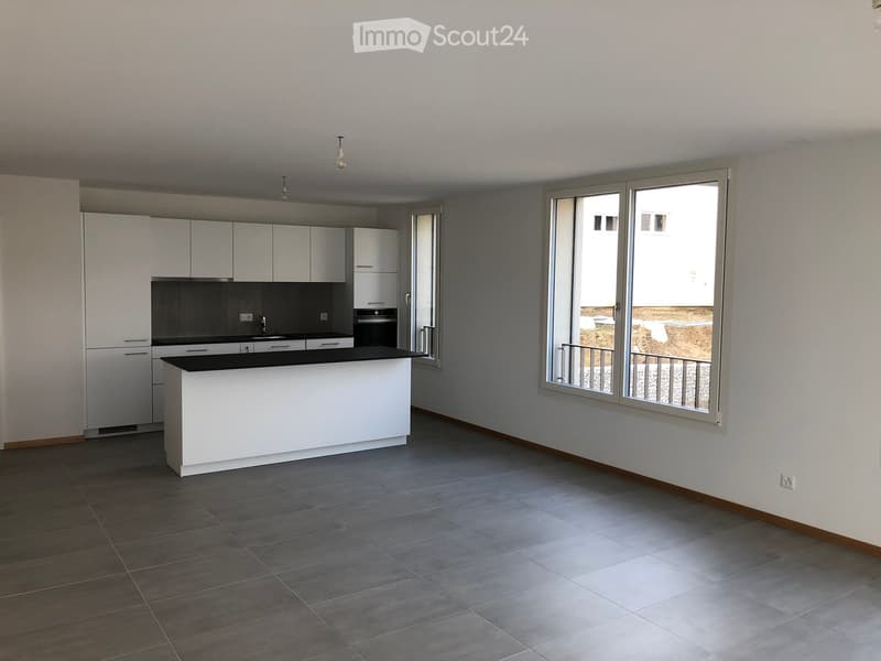 Modern kitchen with white cabinets, black countertops, and a central island. Large windows provide natural light and access to a balcony.