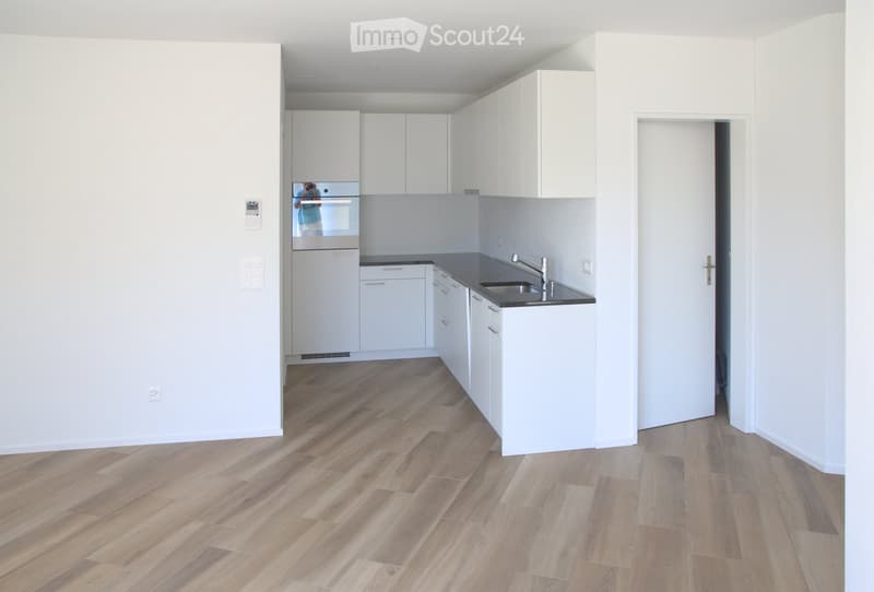 Empty kitchen area with white cabinets, wooden flooring, and a sink, connected to an adjacent unfurnished space.
