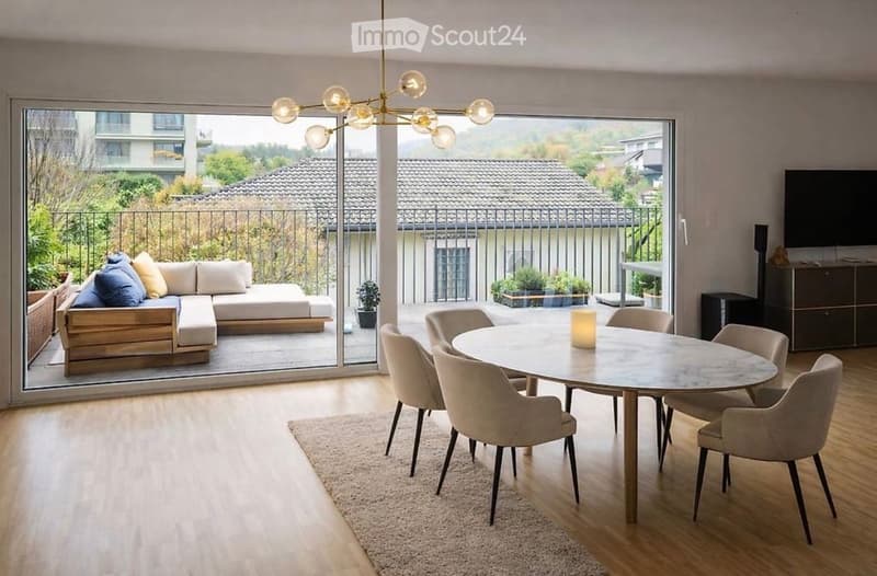 Modern living and dining area with large windows and balcony access, featuring a sofa, coffee table, dining table with chairs, and a television.
