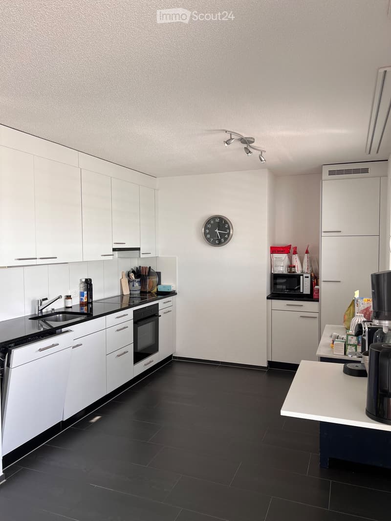 Modern kitchen with white cabinets, black countertops, and stainless steel appliances. Features include a sink, oven, microwave, coffee maker, and a clock on the wall.