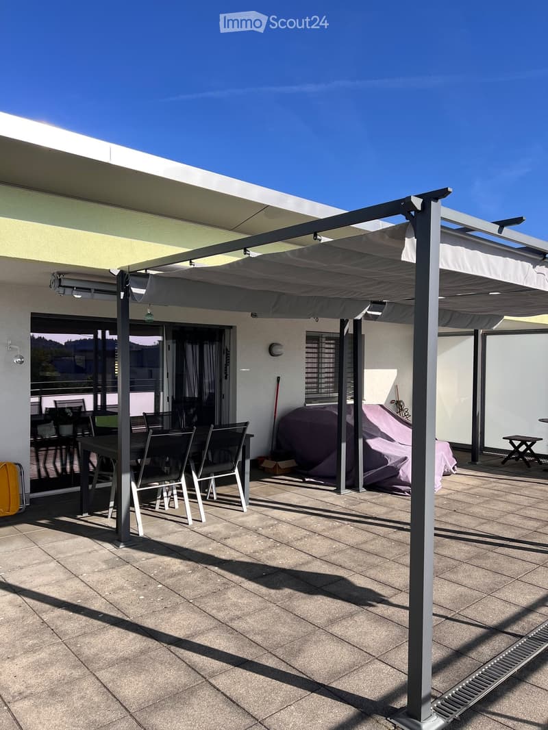 A covered patio with a tiled floor, a dining table and chairs, and a covered area with a retractable awning.