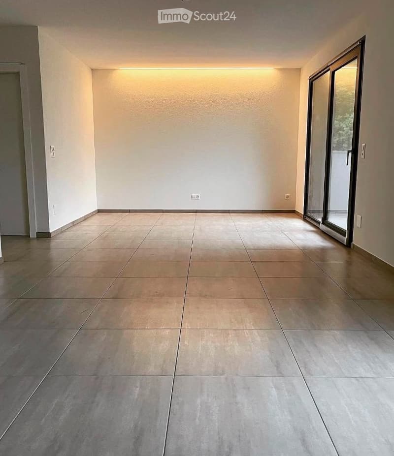 Empty room with tiled floor and large sliding glass doors leading to an outdoor area. The walls are painted white, and the room has recessed lighting.