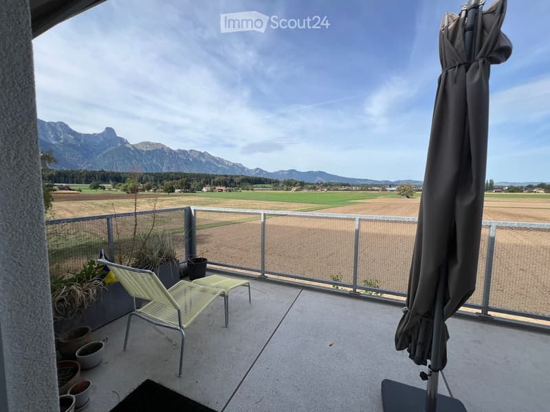 Balcony with a scenic mountain view, featuring a lounge chair, small table, umbrella, and several potted plants.