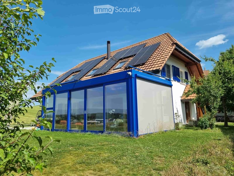 Modern two-story house with solar panels on the roof, large glass extension, and well-maintained lawn.