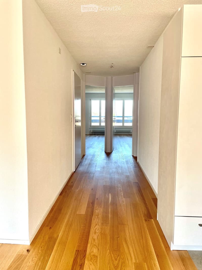 Empty hallway with wooden flooring, white walls, and doors leading to rooms.