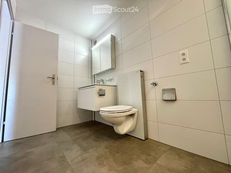 Modern bathroom with white tiled walls, a toilet, a sink with a mirror, and a door with a silver handle.